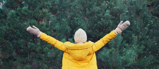 Winter day, happy young woman enjoys snow, warm weather against Christmas tree in snowy green forest