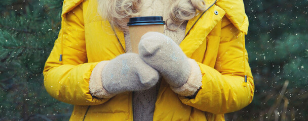 Close up female hand holding cup of hot coffee drink against Christmas tree in winter forest