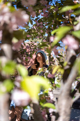Sakura Woman Beret: Young girl sits on bench in spring park with cherry blossoms.