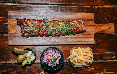 A large piece of meat is on a wooden cutting board with a side of coleslaw