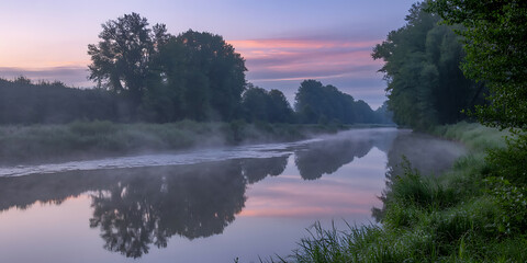 Serene river reflects a pastel-colored dawn sky, surrounded by lush green trees.