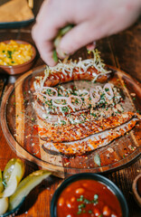 A person is putting food on a plate, including a hot dog, a piece of meat