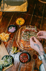 A person is putting toppings on a pizza on a wooden table