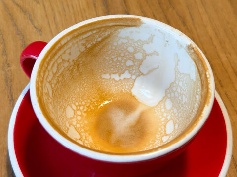 Empty coffee cup with foam traces on red saucer. Warmth, everyday ritual and comfort after morning drink in cozy cafe. - Powered by Adobe