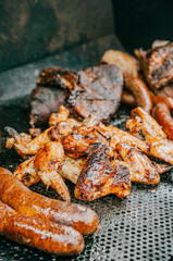 A plate of food with chicken wings, sausage, and ribs on a grill