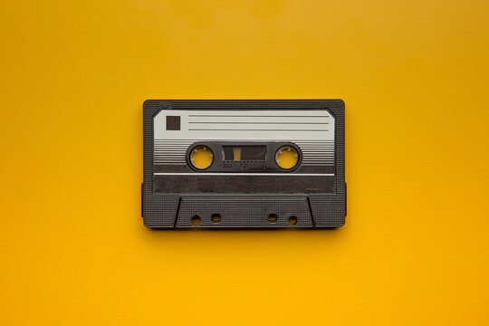 Single vintage black audio cassette tape on bright yellow back