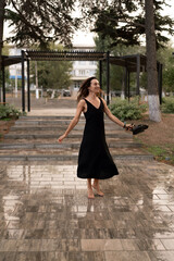 Woman barefoot walking, enjoying wet paved path in park holding shoes feeling free