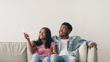 Split System. Satisfied African American woman holding remote control relaxing under the air...