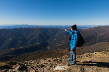 Fototapeta premium Adventurous hiker points toward stunning mountain vistas, inspiring wanderlust and outdoor exploration on a clear day with a vibrant blue sky above