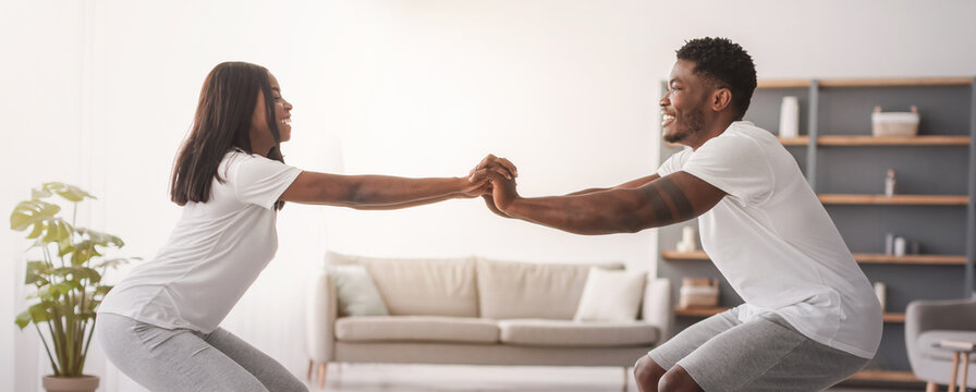 Family Workout. African American Husband And Wife Exercising Doing Syncing Squats Holding Hands, Training Together At Home. Sporty Lifestyle, Couples Fitness Routine, Yoga Balance Exercise Concept