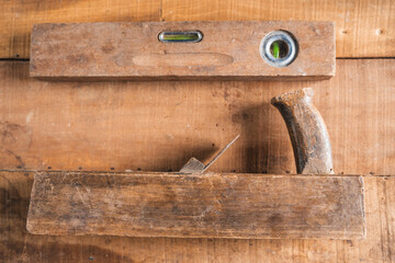 Antique construction tools, such as an old wooden level, a wooden plane, pliers, and a plumb line, are isolated and display an antique charm on a brown wooden wall.