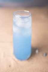 chilled blue beverage in tall glass on sandy beach surface with soft focus background evokes refreshing summer vibes and cool relaxation in tropical setting, light, marine, simplicity, idyllic