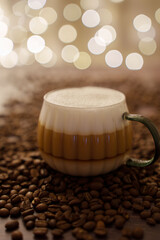 a frothy cappuccino in a stylish glass mug surrounded by coffee beans on a wooden surface, with a background of warm bokeh lights creating a cozy and inviting ambiance, highlight, warmth, intimate