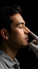 A photorealistic portrait of a young man in post-rhinoplasty recovery, softly lit against a deep black background. The gloved hand and precise lighting emphasize professional care and clinical precisi