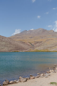 View of the serene turquoise lake reflecting the arid mountain range under a vast blue sky, creating a stunning contrast of color and texture, Lake Kari, Shirak Province, Armenia.