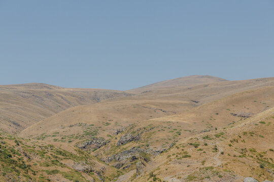 View of undulating, arid hills bathed in the warm glow of the sun, creating a serene landscape under a clear blue sky, Lake Kari, Shirak Province, Armenia.