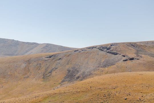 View of sun-drenched hills with muted yellows and browns under a soft, pale sky create a tranquil, arid landscape, Lake Kari, Shirak Province, Armenia.