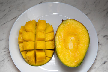 Juicy yellow mango cubes with whole mangoes on a white plate. Vegetarian.