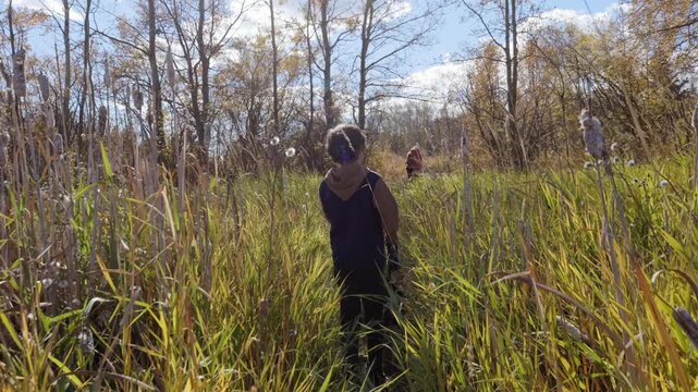 Two boys walking out of tall grass in the woods on a warm sunny day