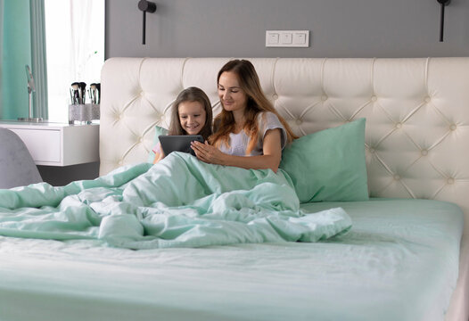 Mom and her little daughter sit in bed after waking up and using their gadgets. Problem of excessive phone and tablet use. Lack of communication between family members in the modern world