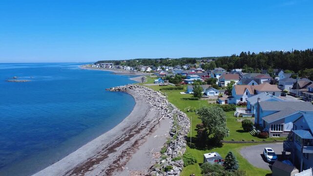 A flight over the beach of the picturesque, eroding coastal village of Saint-Ulric-de-Matane on the banks of the St. Lawrence River under a cloudless blue sky. Quebec, Canada, 2025.