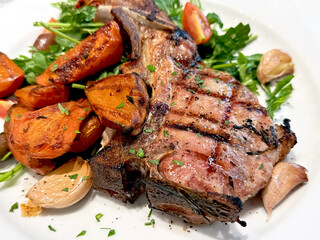 Grilled pork chop with roasted sweet potatoes, garlic, cherry tomatoes and fresh arugula. Gourmet meat dish concept.