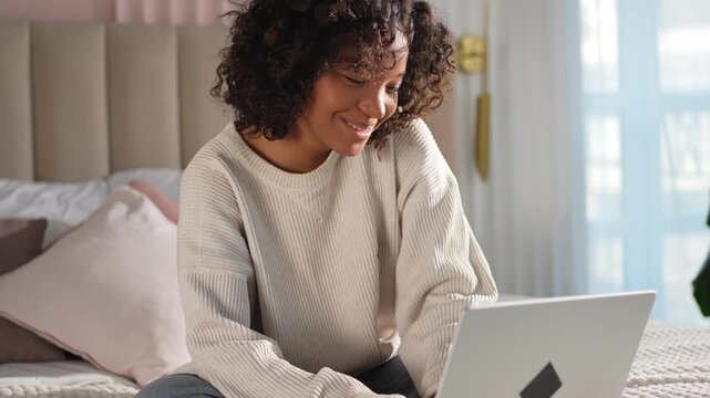 African American girl using laptop in bed at home office typing chatting reading writing email. Young black woman having virtual meeting online chat video call conference. Work learning from home