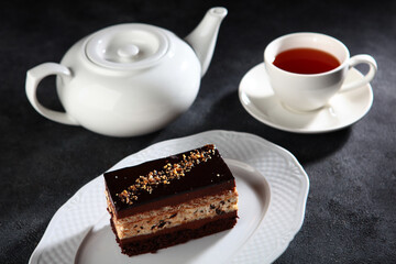 Piece of chocolate cake with tiramisu cream and nutty sprinkles. Chocolate dessert. Cup and teapot made of white porcelain.