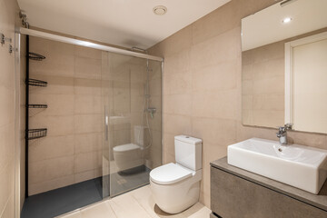 Modern bathroom with a glass shower, white toilet, and sleek sink. Neutral tile walls and floor create a clean, minimalist aesthetic.