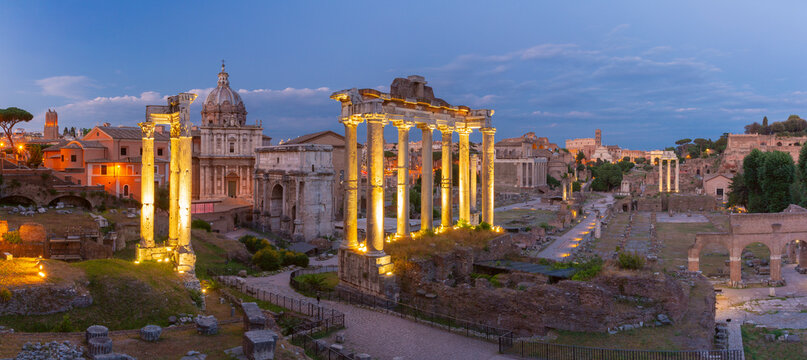 Ancient Roman Forum with lit columns and ruins at sunset in Rome, Italy