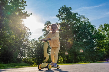 Scooter child. Girl riding scooter toddler. Yellow outdoor activity park road.