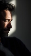 man looking out window with sunlight and shadows, introspective mood