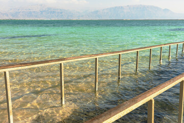 a bridge with a railing extending into the sea, the coast of the Dead Sea