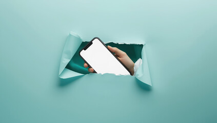 Hand holding a smartphone with a blank white screen emerging from a torn hole in a teal paper background, concept for technology and communication transparent mockup 