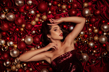 Glamorous red Christmas vibe with elegant model resting among festive baubles and sparkling decorations