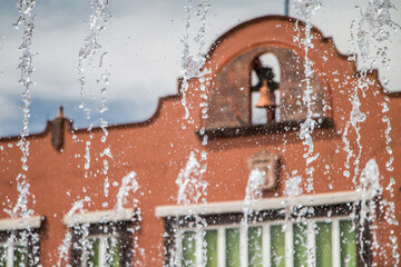 Orange Mexican town building with bell tower and fountain in foreground