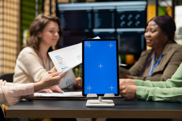 Group of diverse colleagues gathering near isolated copy space on tablet in boardroom, perfect for custom organizational graphics, finance charts or analytics overlays for performance reports.
