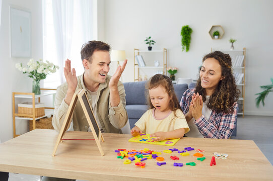 Family parents teach daughter numbers and alphabet during educational game at home. Little child girl practices learning with magnets and chalkboard as parents guide, easing homework. Kids education