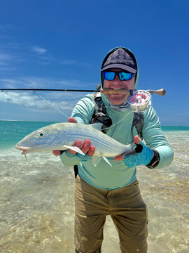 Fly fisherman holding a freshly caught bonefish while standing on the crystal-clear tropical flats of Kiritimati (Christmas Island), Kiribati. This remote Pacific atoll is internationally recognized a