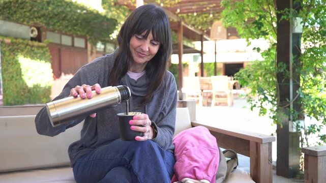 Woman preparing and serving traditional yerba mate outdoors on a sunny terrace