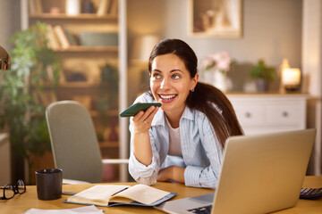 A woman is speaking on her smartphone while seated at her desk in a cozy home office, radiating positivity and joy during her conversation.