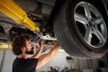 A skilled mechanic examines the undercarriage of a vehicle, using tools to complete essential repairs in a well-lit auto repair shop. The atmosphere is focused and industrious.