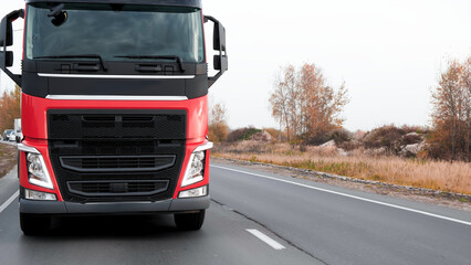 Red Truck is driving on the interstate highway. Close-up of the front of the truck. A column of cars accumulated behind the truck.