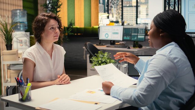 HR manager going over the health insurance and paid time off details, reviewing the salary and package benefits of the employment contract. African american candidate at the job interview. Camera A.