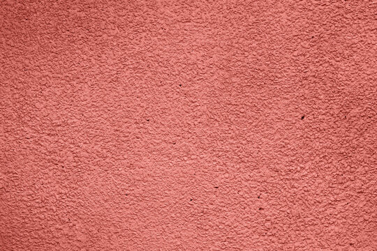 Close-up of rough textured wall painted in burnt sienna color, showing its grainy surface and warm tone. Concept of color of year, color of season, burnt sienna design inspiration