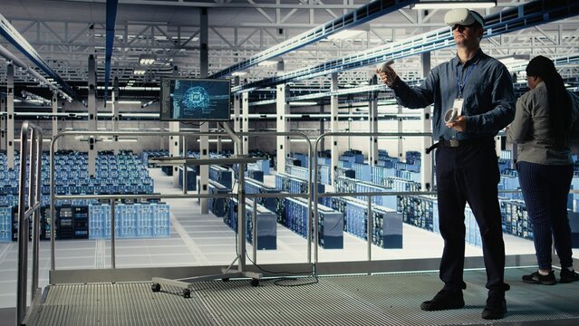 Programmer in server room wearing VR headset optimizing deep learning systems handling tasks. Data center IT specialist adjusting AI model parameters using virtual reality, camera A