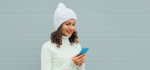 Portrait happy smiling young woman with phone in winter hat, white sweater, girl holding smartphone