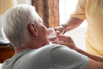 Elderly man drinking water with assistance. Senior care and support. Elderly nursing care and...