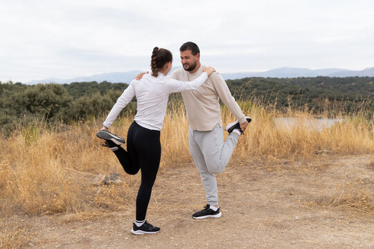 Couple stretching legs outdoors practicing fitness, performing warm-up exercises together in nature