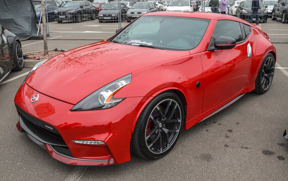 Vibrant red Nissan 370Z sports coupe with distinct headlights, custom multi-spoke dark alloy wheels and a subtle front lip spoiler highlighting dynamic design